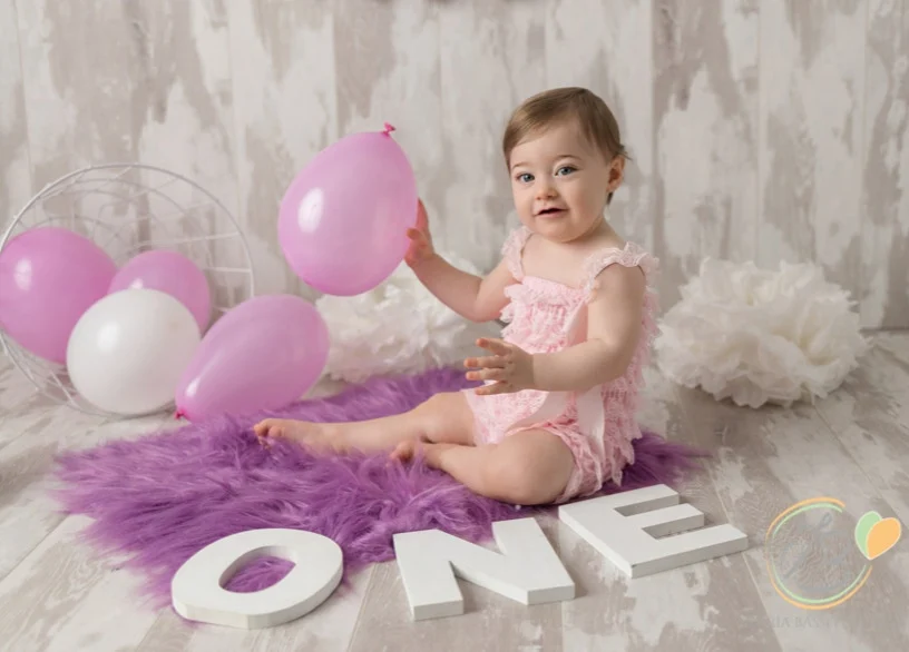 Una bambina seduta tra palloncini rosa e le lettere ONE